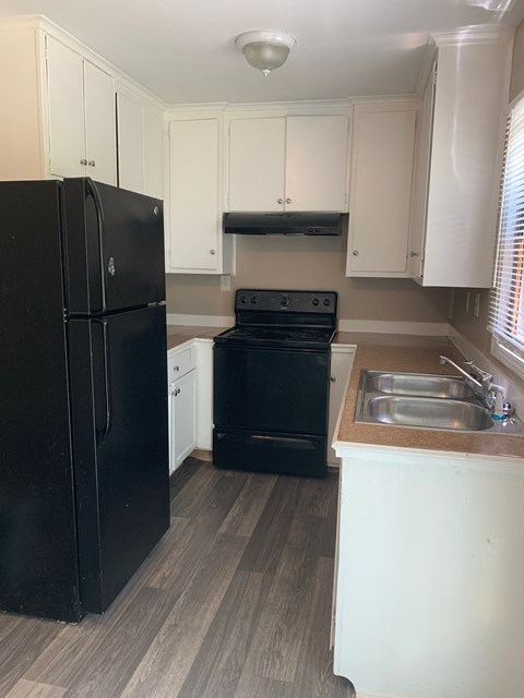 A black refrigerator is in a kitchen with white cabinets.