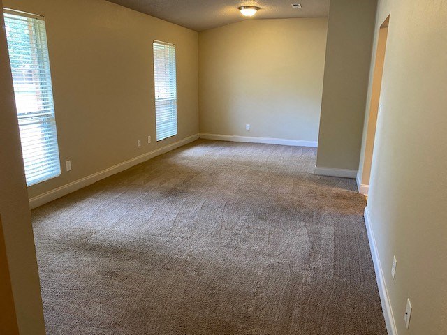 A room with carpeted floor and two windows.