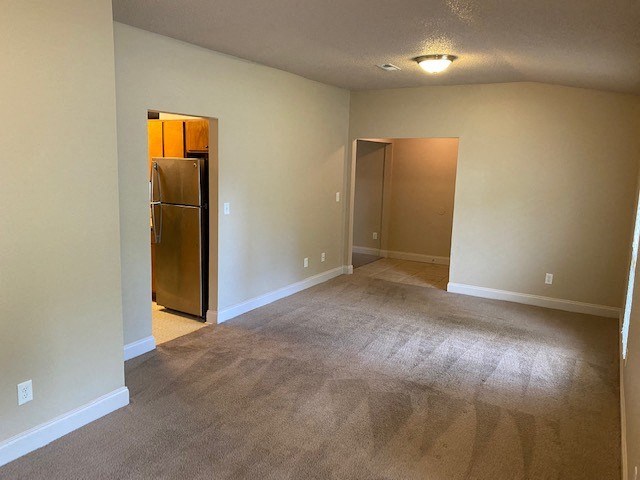 A room with a carpeted floor and a refrigerator in the corner.