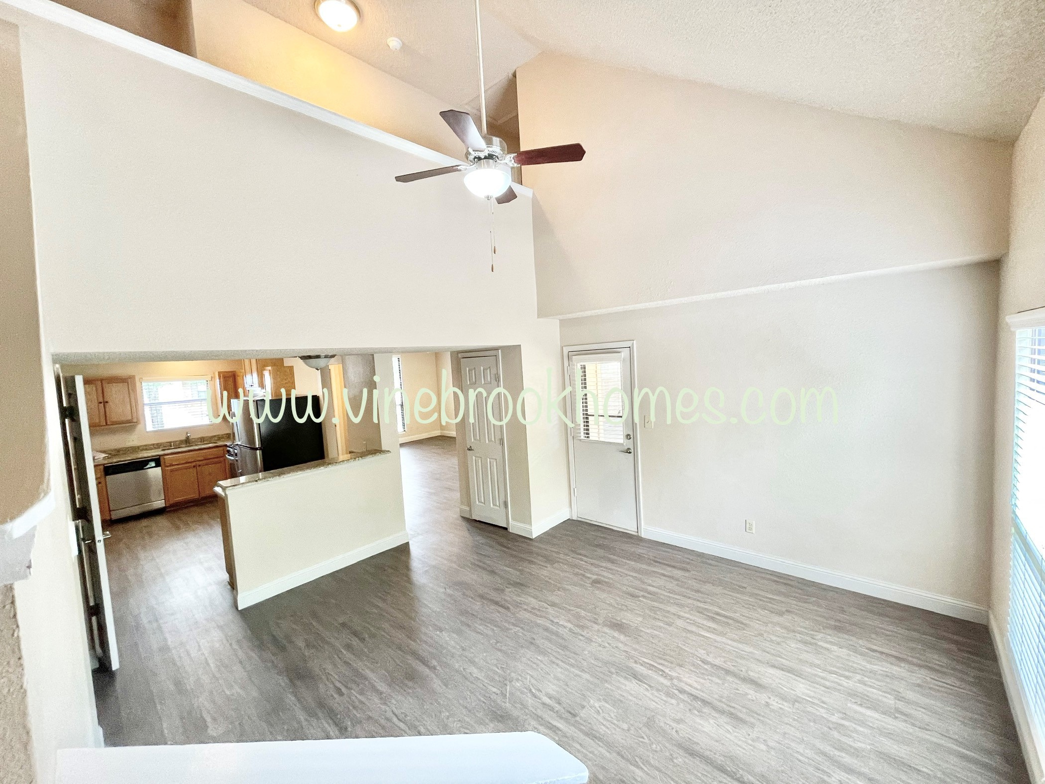 an empty living room with a kitchen and a ceiling fan