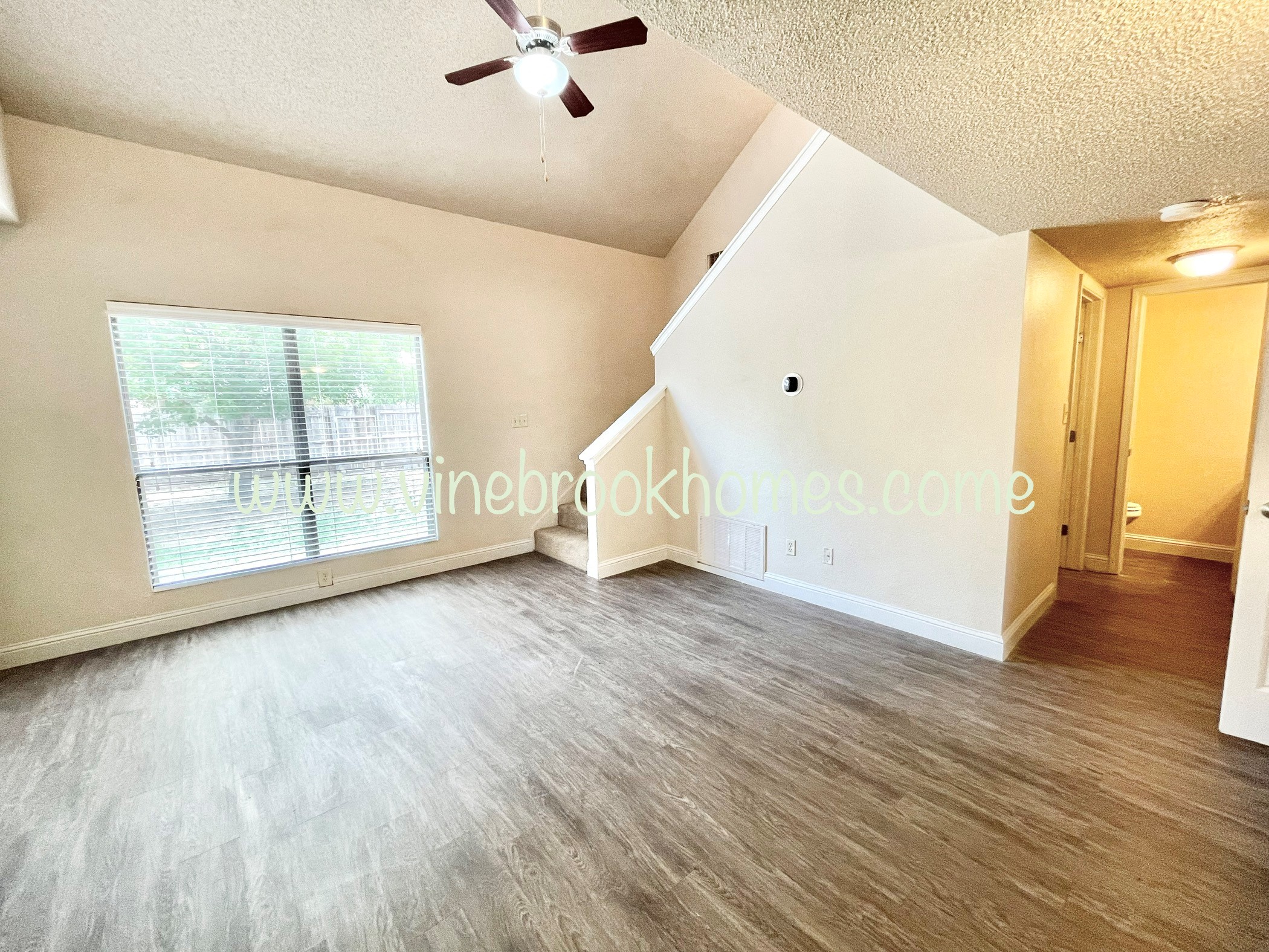an empty living room with a ceiling fan and a large window