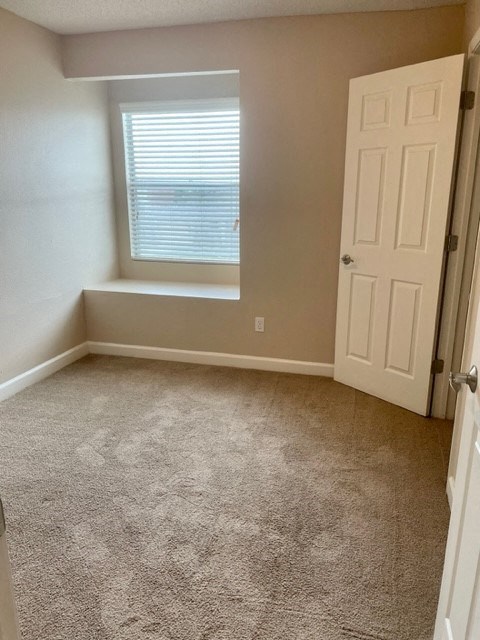 A room with a carpeted floor and a window with blinds.