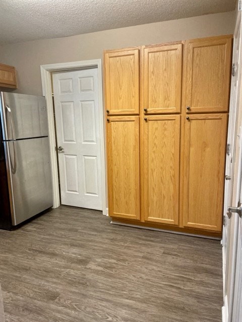 A kitchen with a refrigerator, a white door, and wooden cabinets.