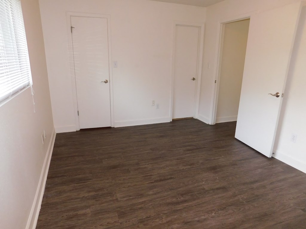 A room with white walls and wood flooring with three doors.