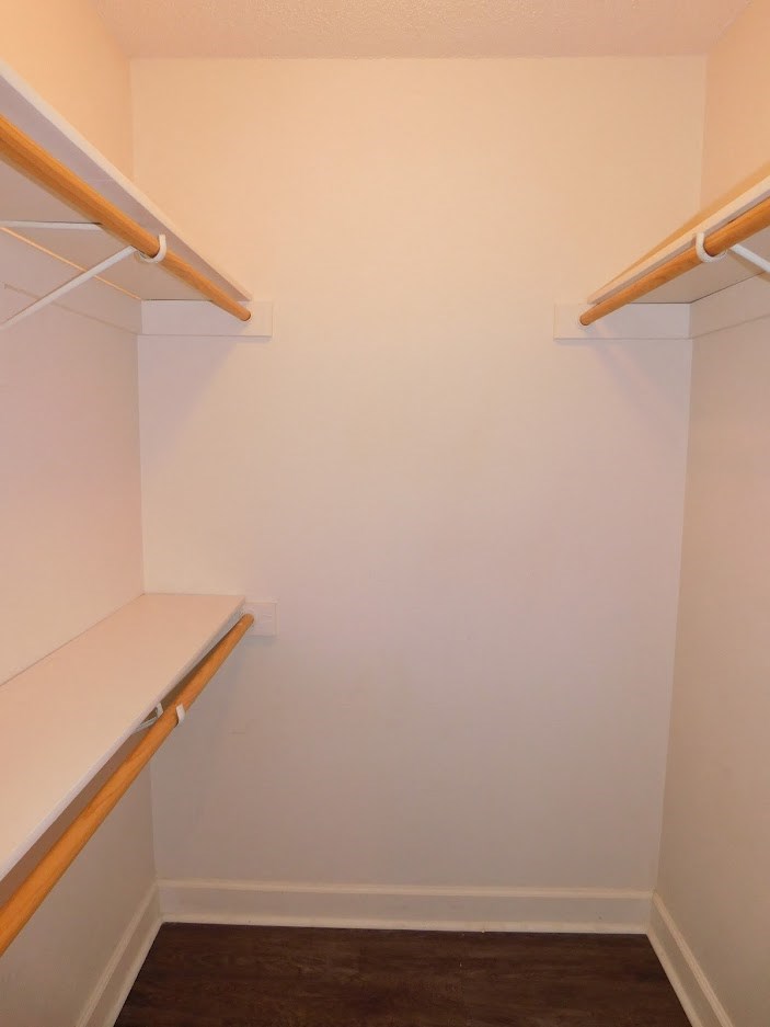 A white closet with two shelves and a wooden floor.