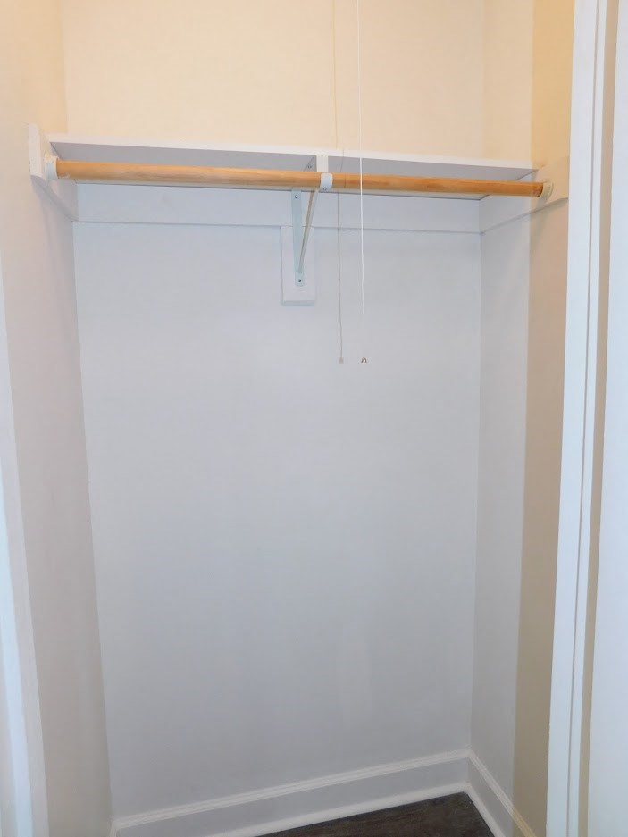 A white closet with a wooden rod and hooks.