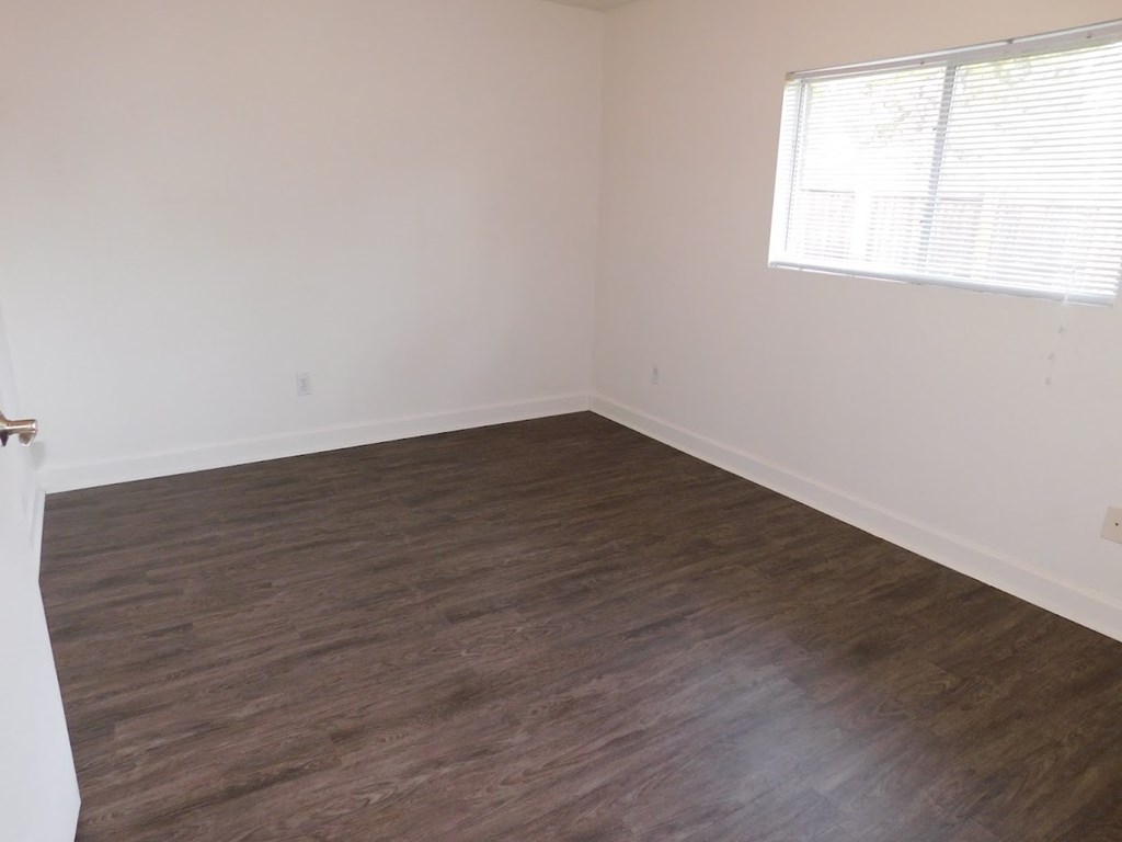 A room with wooden flooring and a window with blinds.