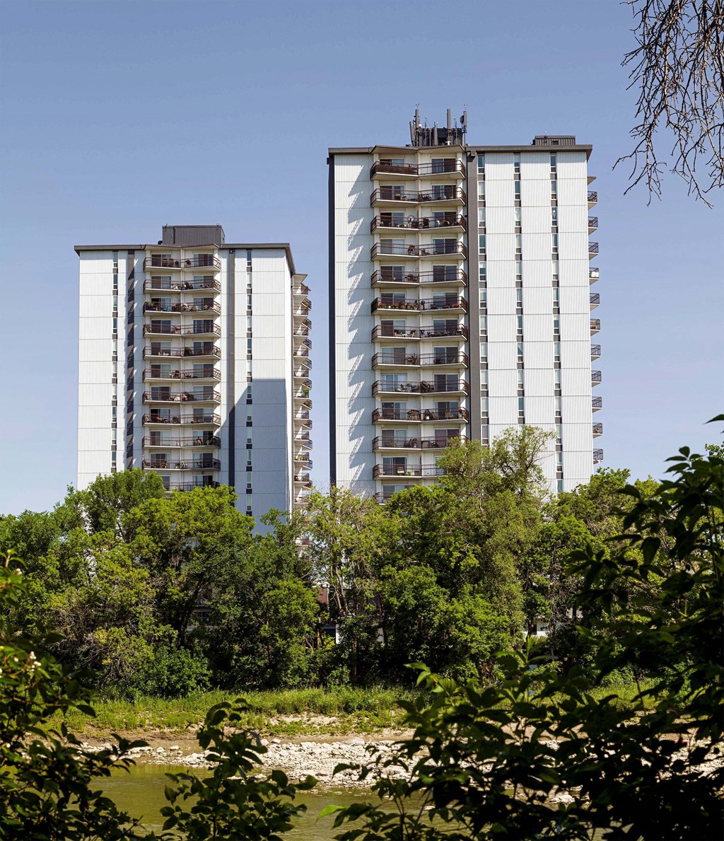 two tall buildings with trees in the foreground and a river
