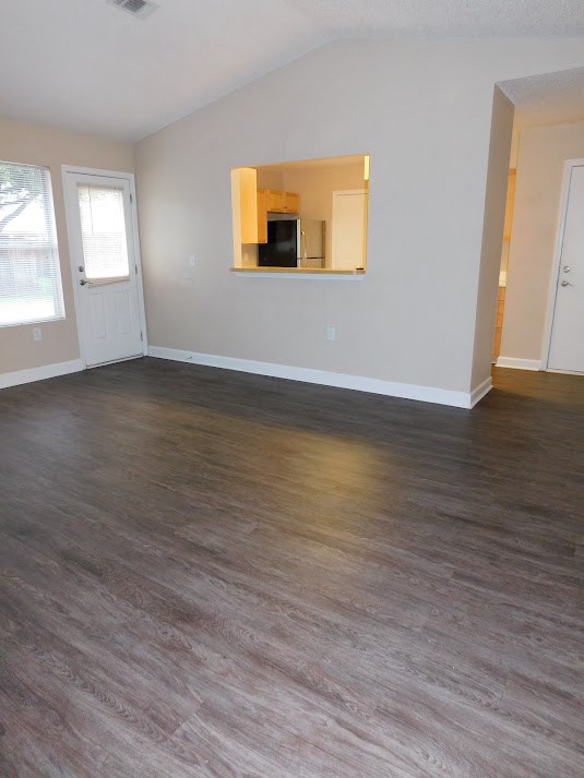 an empty living room with wood floors and a kitchen