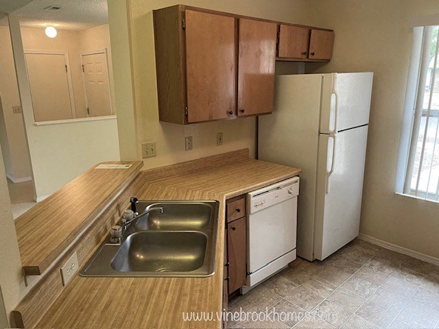 A kitchen with a white refrigerator, a wooden counter top, and a white dishwasher.