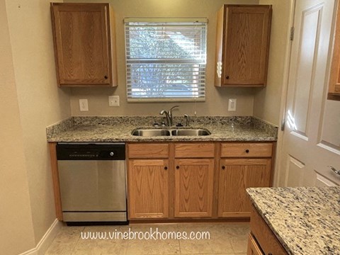 A kitchen with a granite counter top and wooden cabinets.