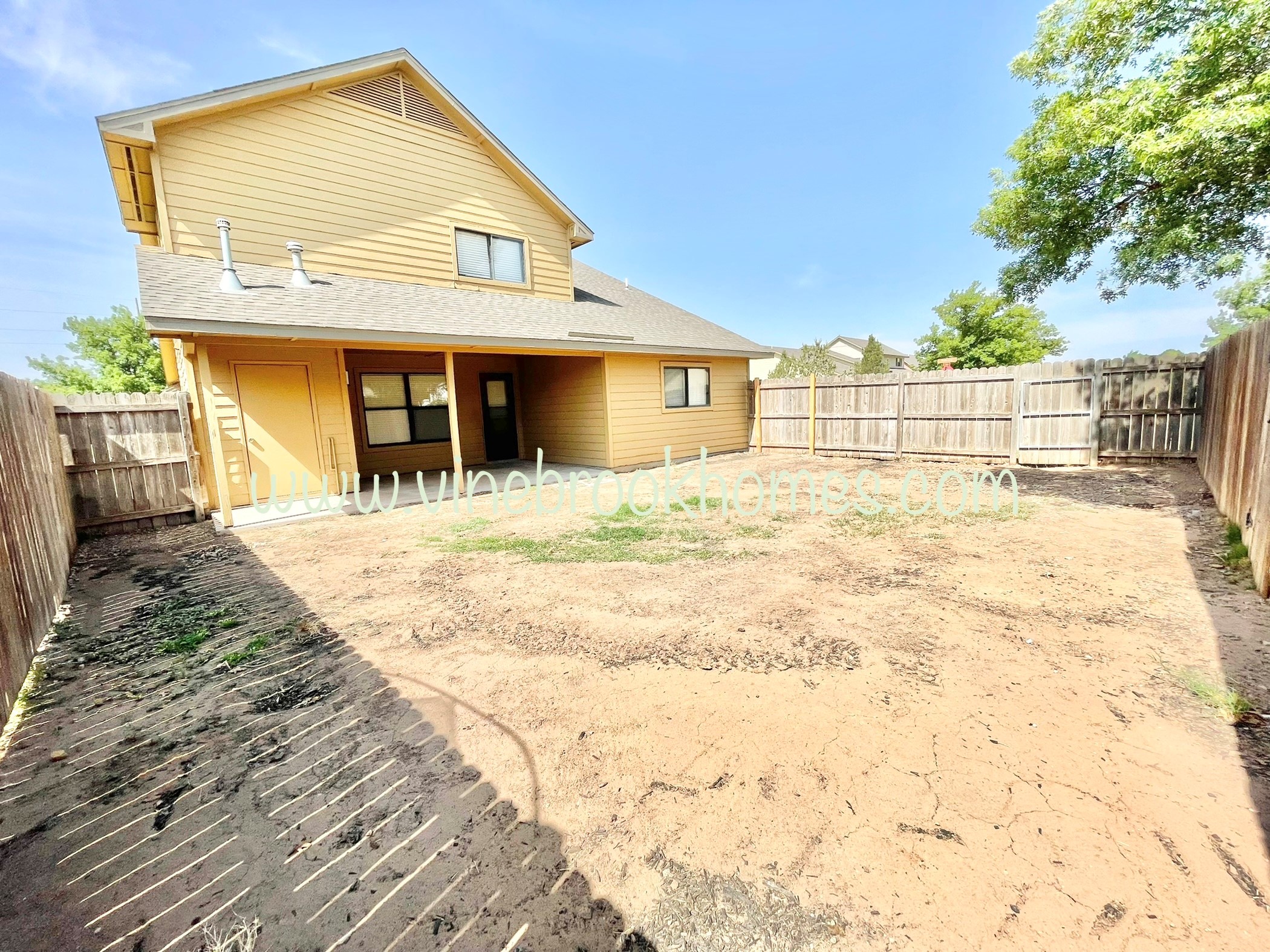 a backyard with a yellow house and a wooden fence