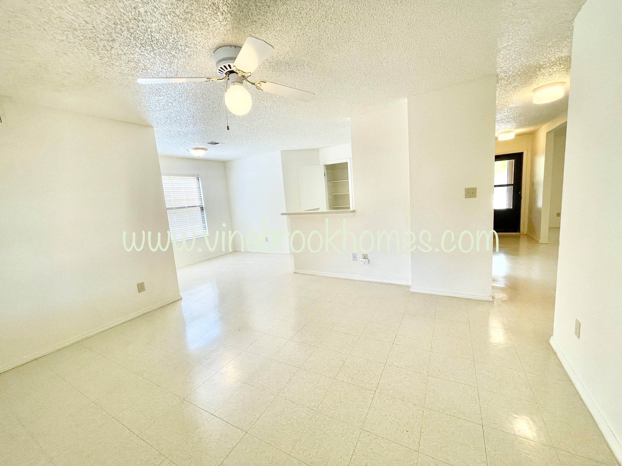 an empty living room with a kitchen and a ceiling fan