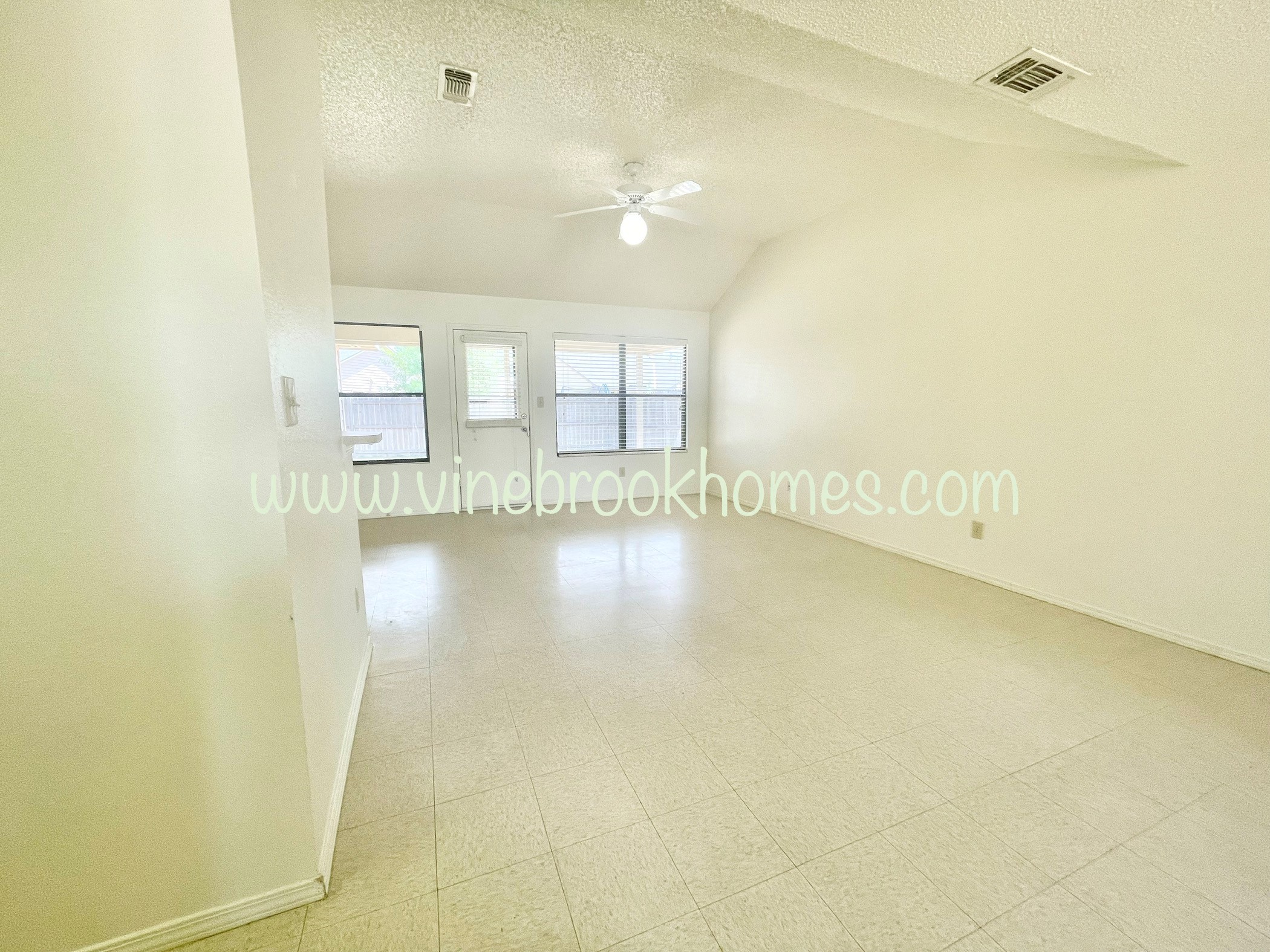 a large white living room with a ceiling fan and windows
