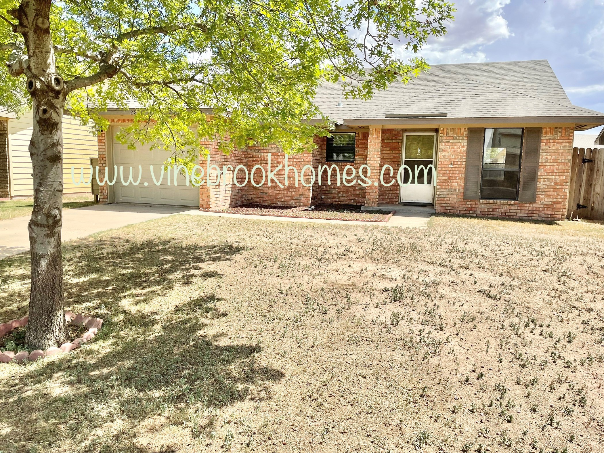 a large yard in front of a brick house with a tree