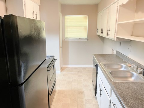 A black refrigerator is in a kitchen with a sink and a window.