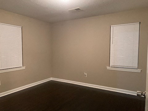 an empty room with two windows and a wooden floor