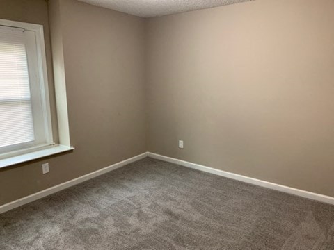 A room with a carpeted floor and a window with blinds.