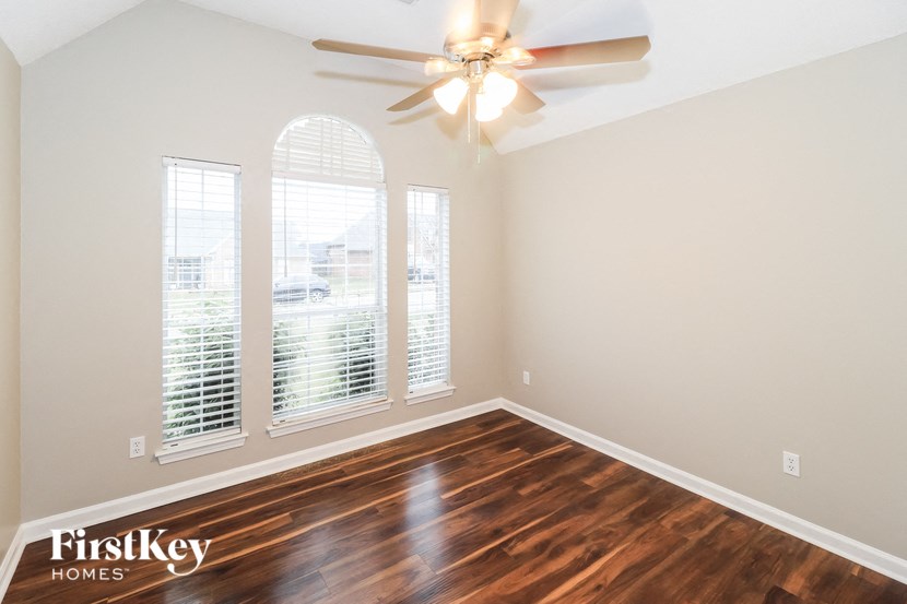 an empty living room with a ceiling fan and three windows