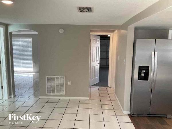 A kitchen with a refrigerator, tiled floor, and a door leading to another room.