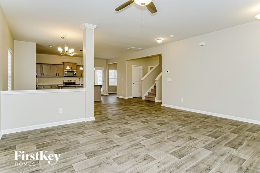 A spacious living room with a wood floor and a staircase in the background.