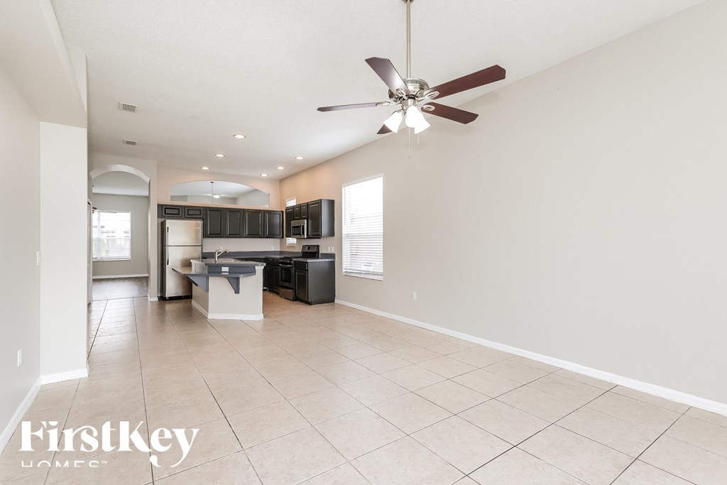 A spacious room with a fan and a kitchen area in the background.