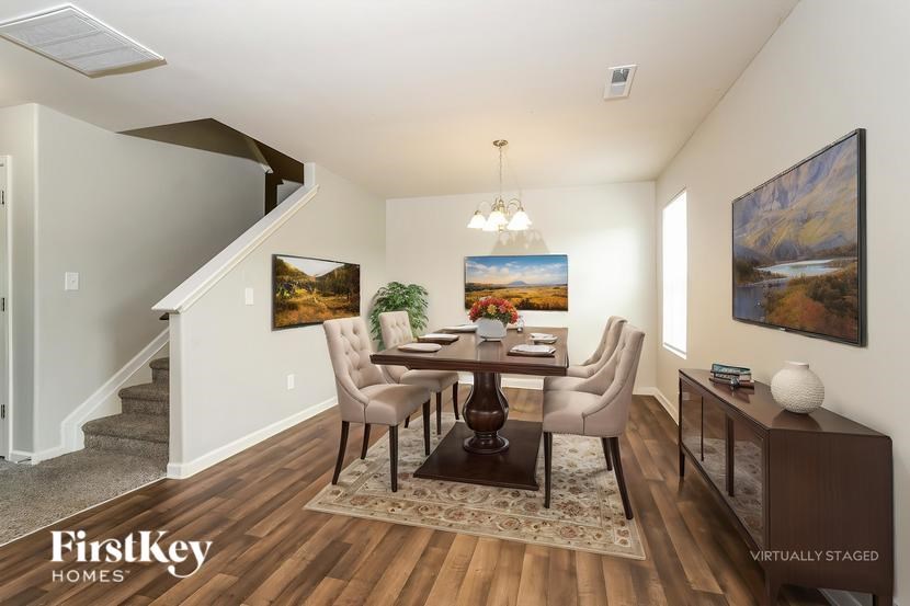 A dining room with a wooden table and chairs, a painting on the wall, and a rug on the floor.