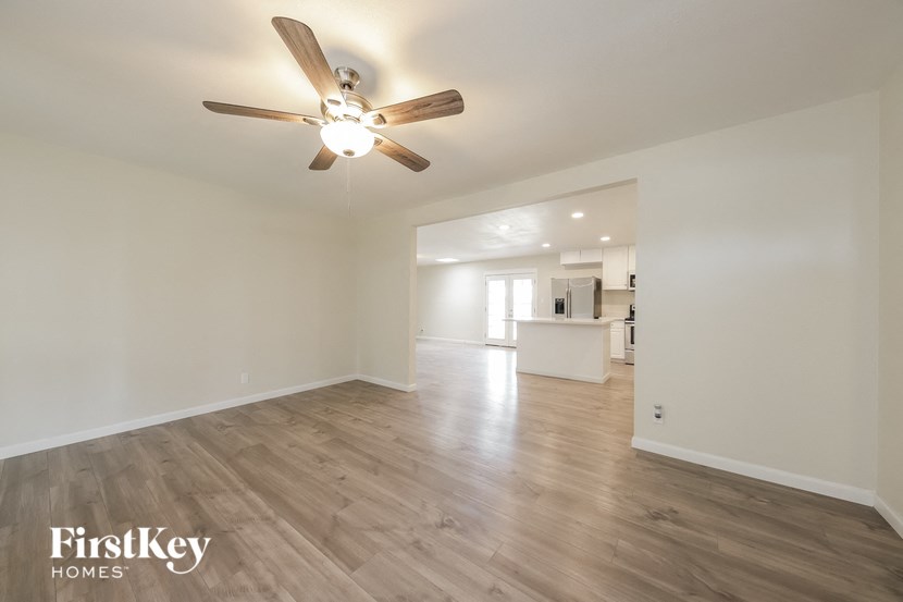 an empty living room with a ceiling fan and a kitchen