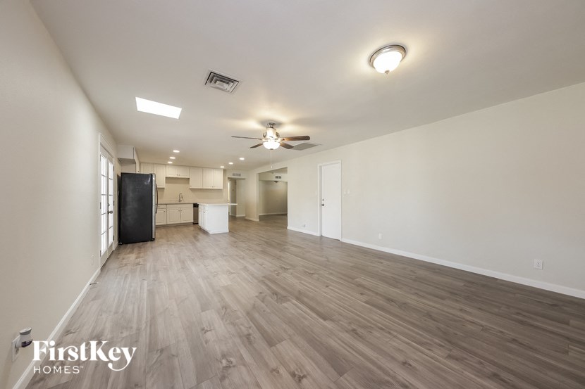the living room and kitchen of an apartment with wood flooring and a ceiling fan