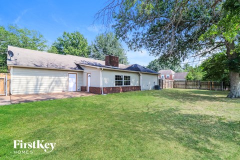 A house with a white exterior and a grey roof is surrounded by a grassy yard.