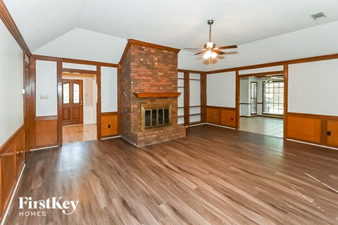 A spacious living room with wood flooring and a brick fireplace.