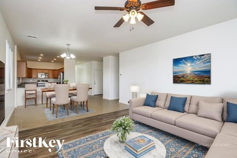A living room with a beige couch, a dining table with chairs, a ceiling fan, and a painting on the wall.