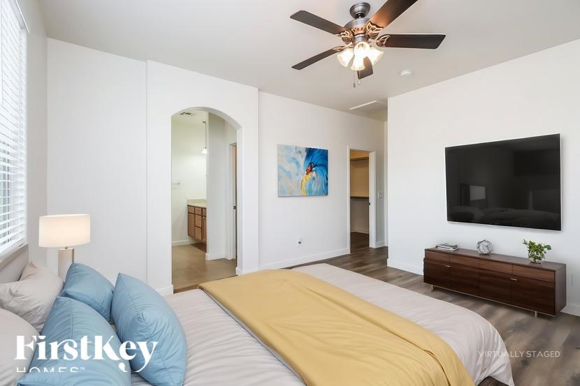 A bedroom with a bed, a ceiling fan, and a painting on the wall.