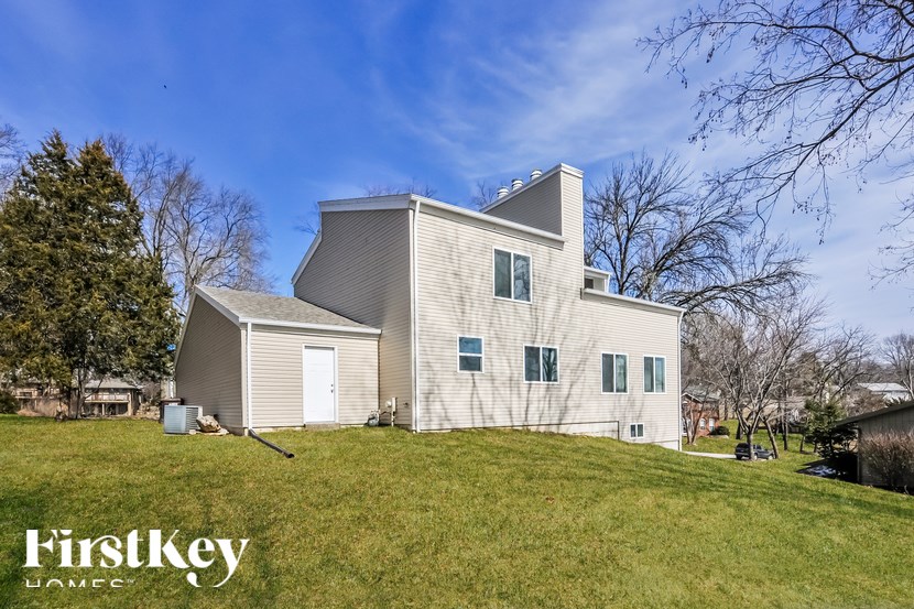 A large white house with a grey roof and a chimney is surrounded by a grassy lawn.