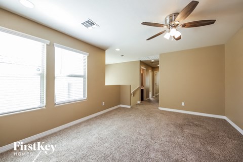 a carpeted living room with a ceiling fan and two windows