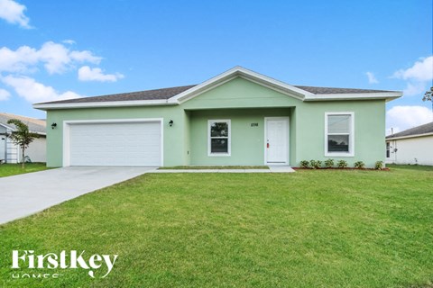 A green house with a white garage door and a white front door.