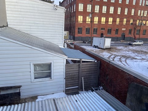 A view of a snowy rooftop with a white house and a red brick building in the background.