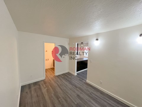 A room with a wooden floor and white walls, with a doorway leading to another room.