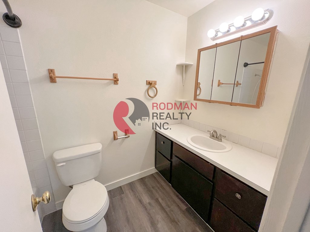A white toilet sits in a bathroom with a wooden cabinet and a mirror above it.
