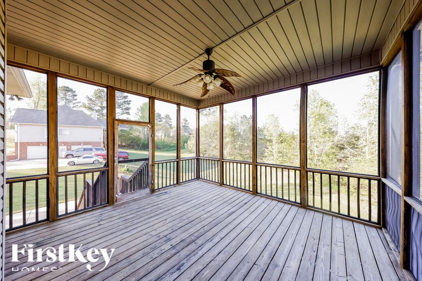A wooden deck with a ceiling fan and a view of a house and trees.