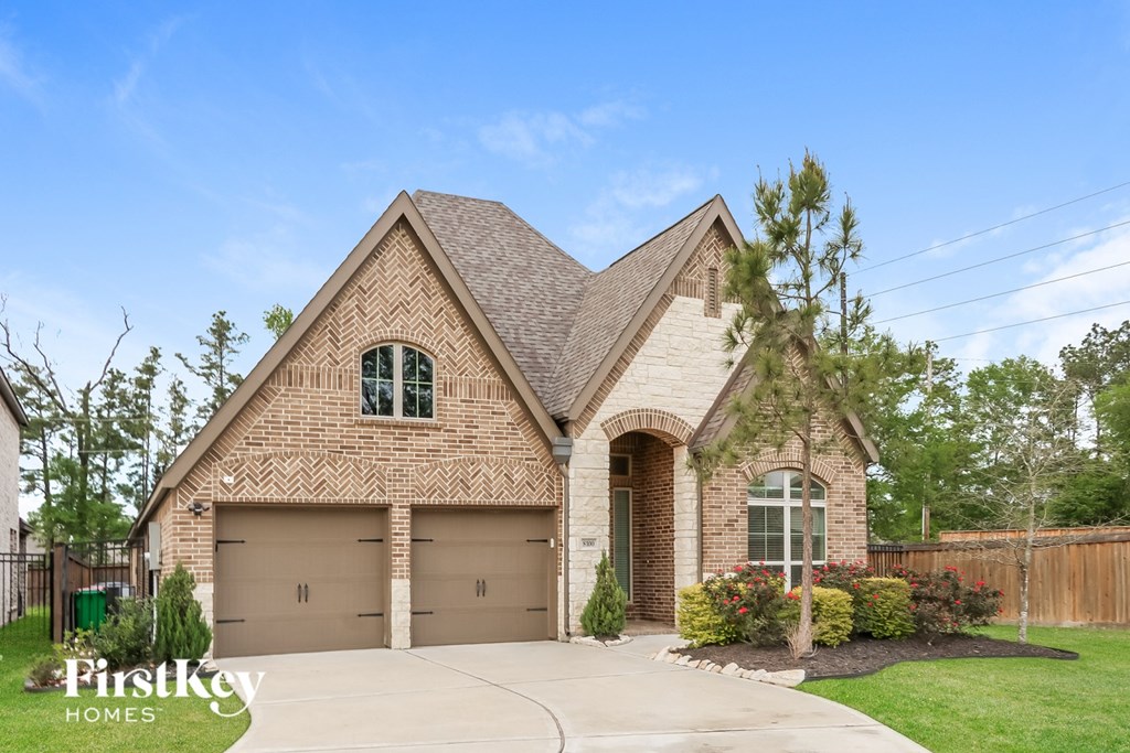 A brick house with a garage and a tree in front.