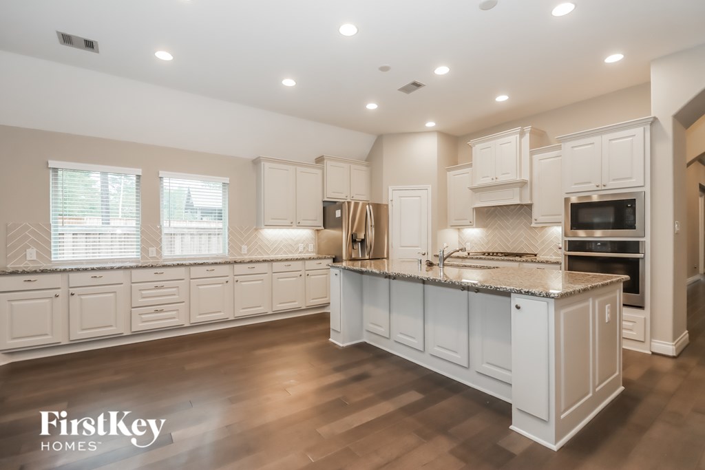 A spacious kitchen with white cabinets and a wooden floor.