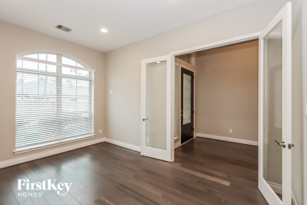 A room with a wooden floor and a large window with blinds.