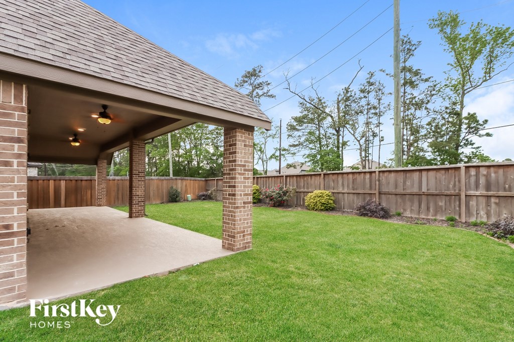 A covered patio area with a grassy lawn and a wooden fence.