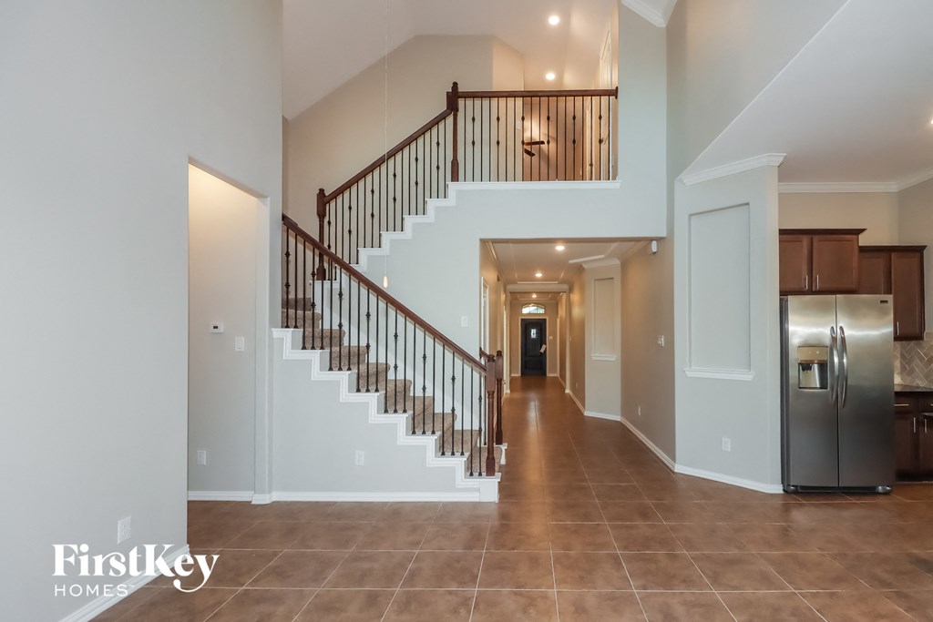 the foyer and staircase of a modern home with a stainless steel refrigerator