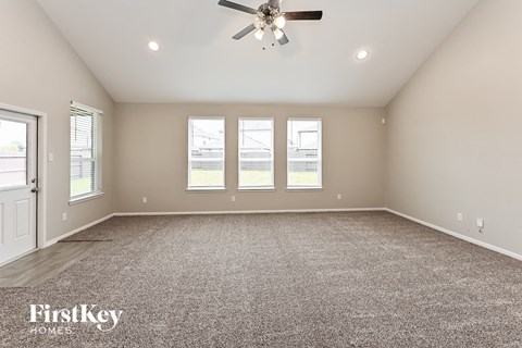 A spacious room with a carpeted floor, a ceiling fan, and three windows.