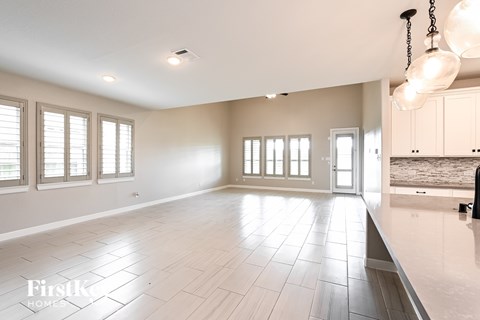 A spacious room with tiled flooring and a kitchen area in the background.