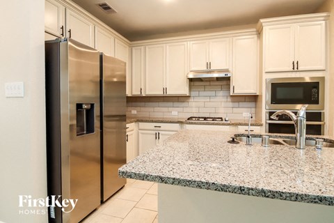 a kitchen with white cabinets and granite counter tops and stainless steel refrigerator