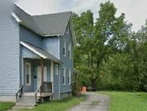 A blue house with a porch and a tree in front.