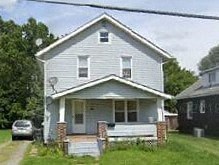 A two-story house with a porch and a car parked in front.